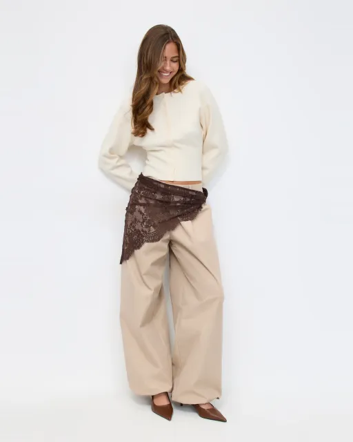 Fashion model in complete editorial outfit with tailored trousers and lace wrap